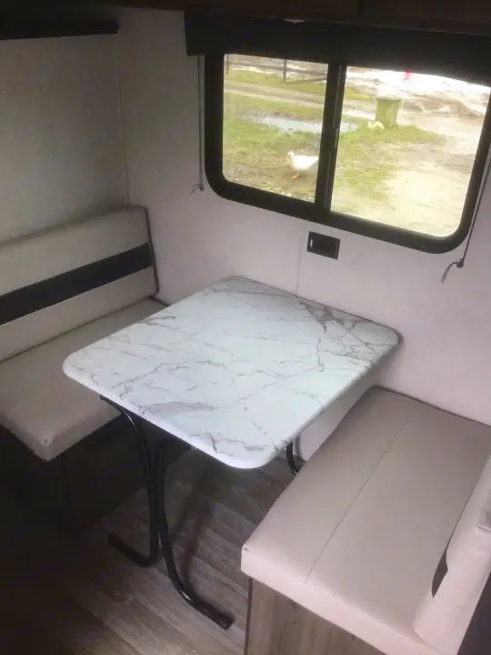 Cozy RV rental dinette with a faux marble table & plush benches. A white duck is visible outside the window.. Coachmen Clipper 2020