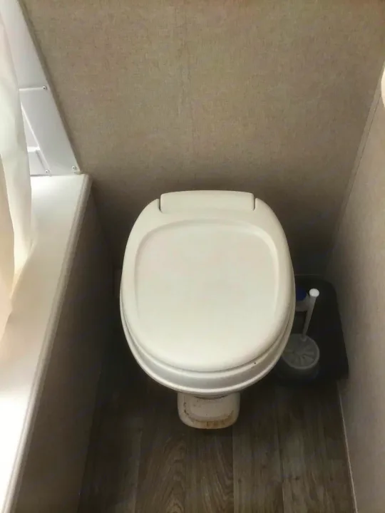 Compact RV rental bathroom with white toilet, shower, and toilet brush on wood-look floor.. Coachmen Clipper 2020