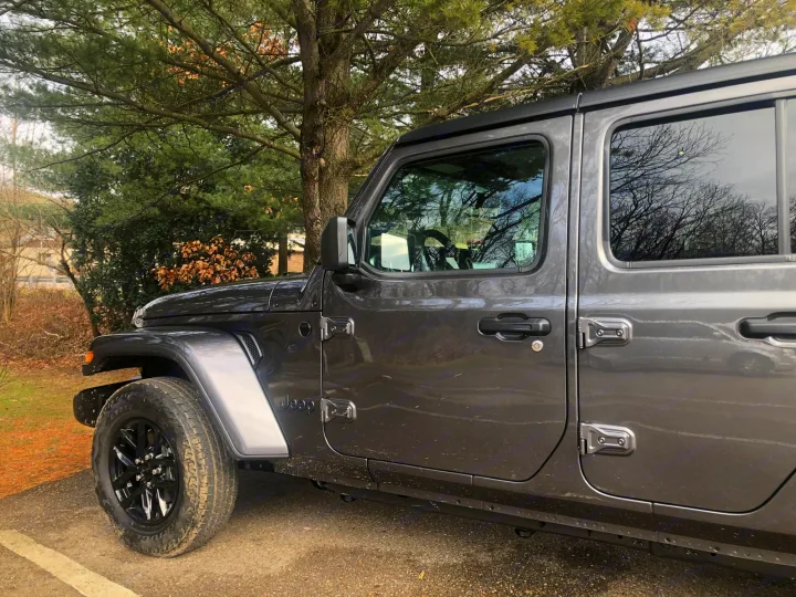 Dark gray 4-door Jeep Wrangler parked outdoors under trees. Rugged vehicle for adventures, a unique alternative to RV rental.. Jeep Gladiator 2021