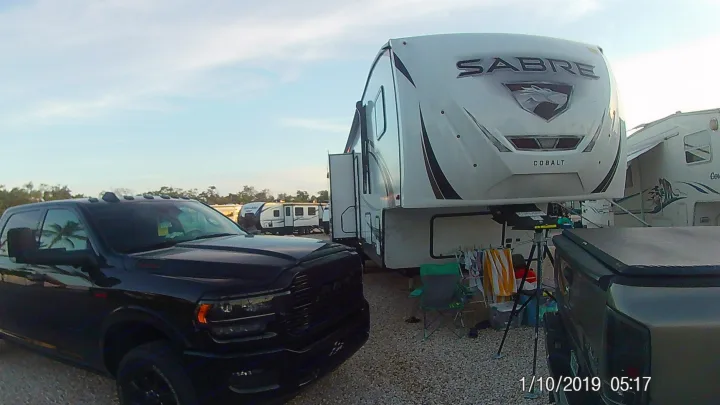 Experience rv rental: A black Ram truck fronts a white Sabre Cobalt fifth-wheel RV at a gravel campsite setup.. Forest River Sabre 2021