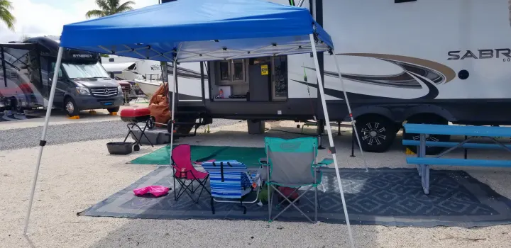 Comfortable RV rental camping setup under a blue canopy with outdoor rug, chairs, and grill, perfect for leisure.. Forest River Sabre 2021