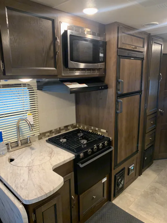 RV rental kitchen: compact space with sink, stove, microwave, fridge, and dark wood cabinets. Ideal for travel cooking.. Forest River Coachmen Prism 2020