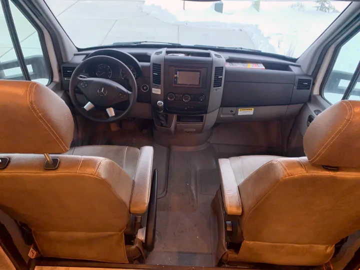 RV rental interior: View of the spacious front cabin with two brown captain's chairs, dashboard, and steering wheel, looking out to a snowy scene.. Forest River Coachmen Prism 2020