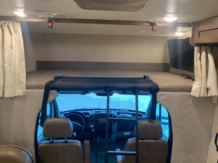 Inside an rv rental: View of the cab-over bunk bed with safety net and ladder, leading to the driver's cockpit.. Forest River Coachmen Prism 2020