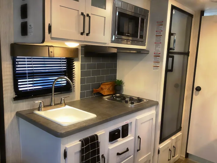 Modern RV rental kitchen with sink, 2-burner stove, microwave, and fridge for travel.. Other Other 2021