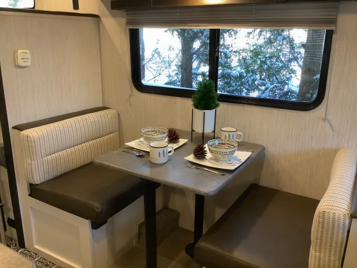 RV rental dinette setup with a cozy table, snow-covered trees outside. Ideal for a relaxing meal inside.. Other Other 2021