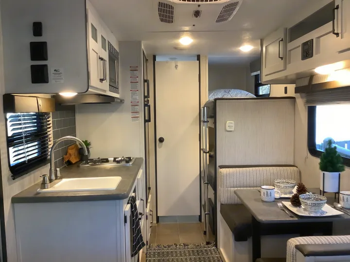 Modern RV rental interior with a well-equipped kitchen, cozy dinette, and bunk beds for comfortable travel.. Other Other 2021