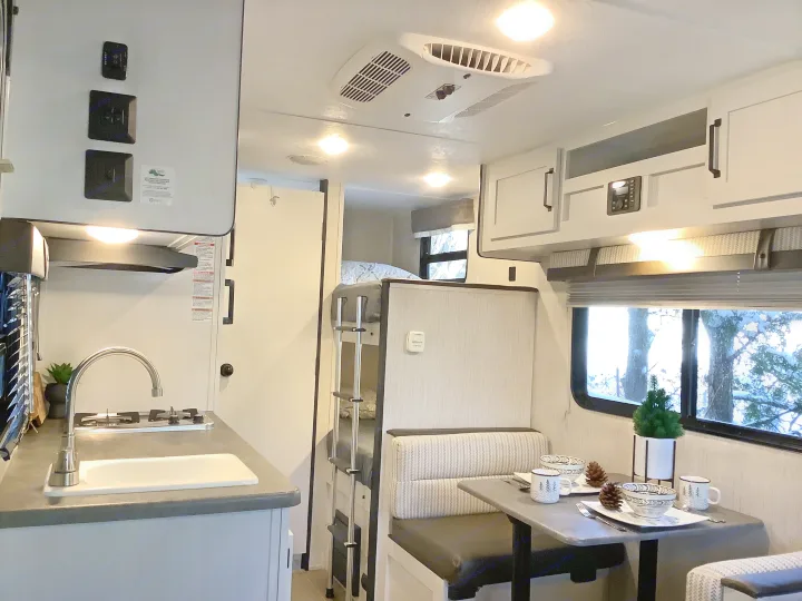 Step into this cozy RV rental! Bright interior with kitchen, dining nook, bunk beds, and a snowy winter view outside.. Other Other 2021