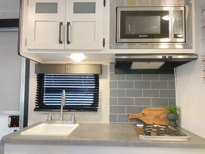 Modern RV rental kitchen featuring a microwave, sink, and cooktop with stylish gray tile backsplash.. Other Other 2021