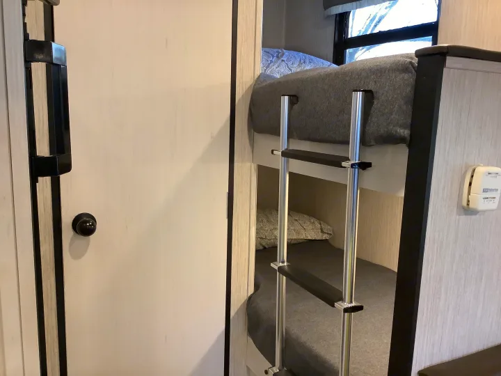 Inside an RV rental, showing a cozy bunk bed sleeping area with a ladder, a door, and a wall-mounted thermostat.. Other Other 2021