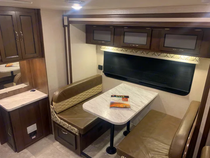 This RV rental features a cozy dinette with upholstered benches, a table, and convenient overhead storage cabinets.. Forest River Coachmen Prism 2020
