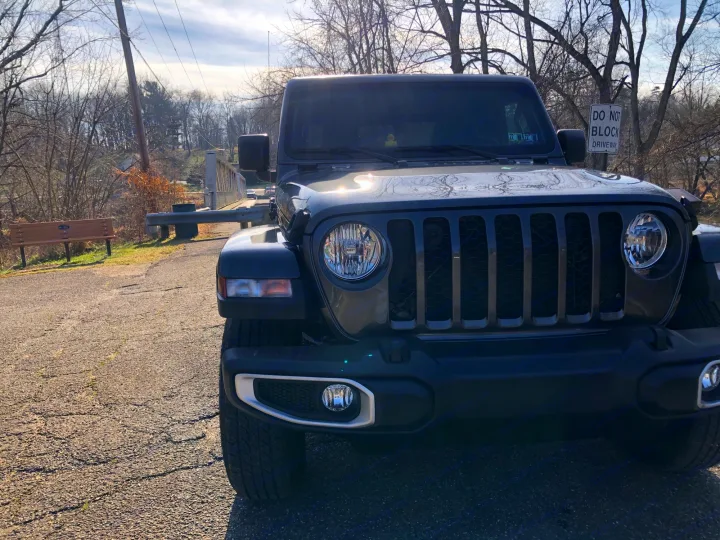 Front view of a dark grey Jeep Wrangler on an asphalt road by a bridge and trees. Consider RV rental for trips.. Jeep Gladiator 2021