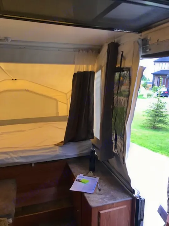 Sideways view of an RV rental interior: a fold-out bed with window insulation & curtains, next to a countertop.. Forest River Other 2017
