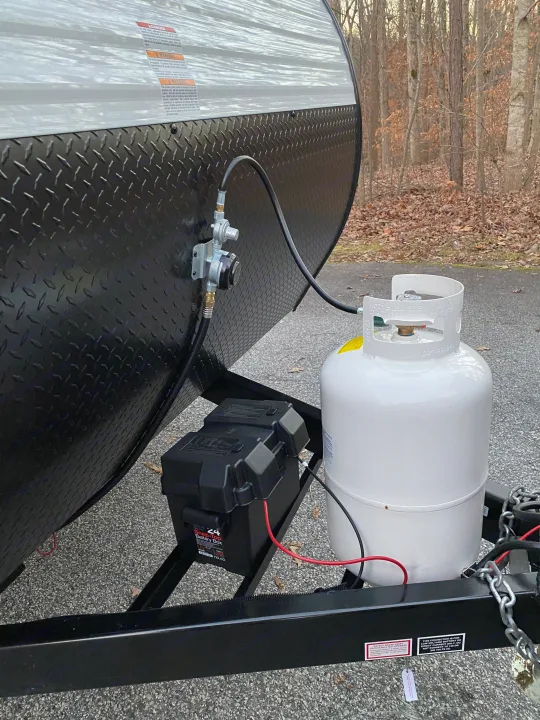Front of an RV rental trailer showing a white propane tank, black battery box, and gas regulator connected for use.. Highland ridge 19bh 2022