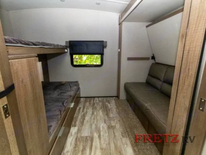 RV rental interior showing bunk beds on the left, a window, and a sofa on the right, providing versatile sleeping and seating.. Grand Design Imagine 2020