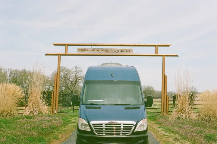 A blue RV rental sits before the "LUCKY SAILOR HORSE & CATTLE CO." gate on a clear day at the ranch.. Freightliner Sprinter 2007