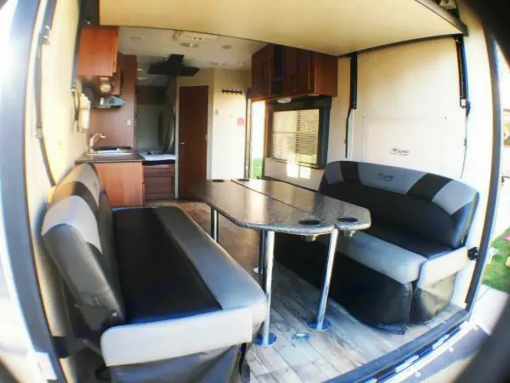 Inside this rv rental: a well-equipped kitchen, dining table with cup holders, and comfortable black & grey benches.. Pacific Coachworks Rage'N 2015