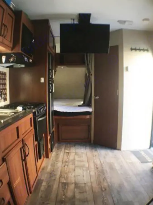 Spacious RV rental interior: well-equipped kitchen, ceiling TV, cozy bed area, and wood-style floor.. Pacific Coachworks Rage'N 2015