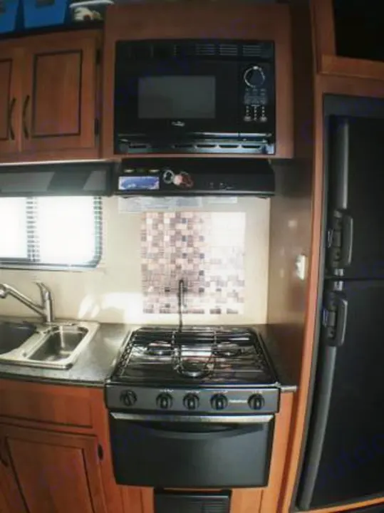 RV rental kitchen: compact space with microwave, gas stove, sink, and refrigerator, ideal for travel cooking.. Pacific Coachworks Rage'N 2015
