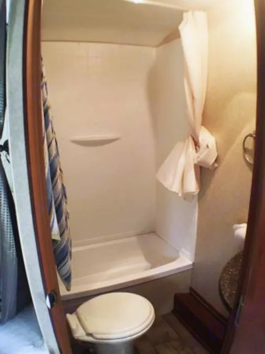 For your RV rental, this clean bathroom includes a shower stall and toilet, providing comfort on the go.. Pacific Coachworks Rage'N 2015