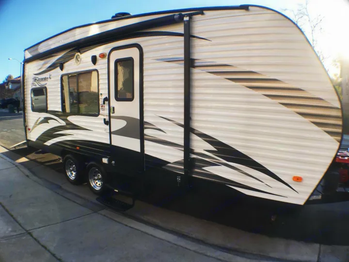 White travel trailer RV, sleek black graphics, extended awning. Great for your next rv rental. Shows side, door, windows, and wheels.. Pacific Coachworks Rage'N 2015