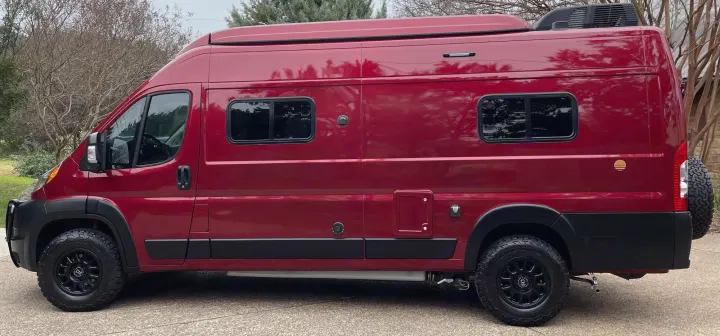 This robust, dark red RV rental camper van is ready for adventure. Side view shows off-road tires, custom windows & rooftop unit.. Winnebago Solis 2021