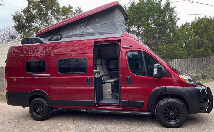 Striking red rv rental camper van with pop-top extended. Open side door reveals custom interior. Equipped for adventure with off-road tires.. Winnebago Solis 2021