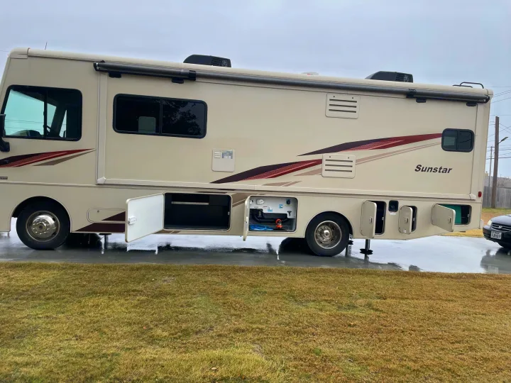 Spacious beige Sunstar motorhome, parked on wet pavement with storage doors open. Perfect for your next RV rental adventure.. Winnebago Sightseer 2019