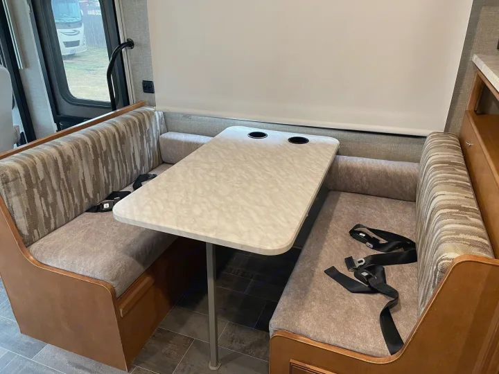 View of an RV rental's dinette: two patterned bench seats, a central table with cupholders, and floor-mounted seatbelts.. Winnebago Sightseer 2019