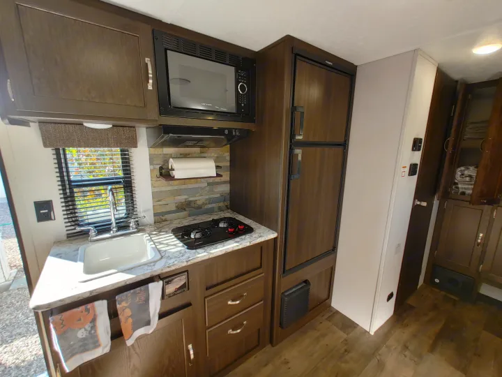 Inside this RV rental: a modern compact kitchen featuring dark wood cabinets, microwave, refrigerator, stove, and sink.. Keystone RV Springdale 2020