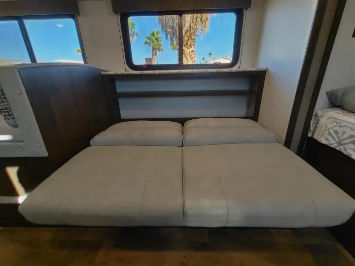 Comfortable RV rental interior with a convertible bed, shelves, and bright windows showing palm trees.. Keystone RV Springdale 2020