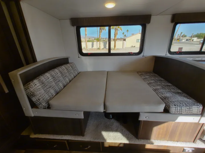 RV rental's dinette converts to a bed, with patterned cushions and sunny window views.. Keystone RV Springdale 2020