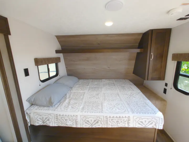 Cozy RV rental bedroom featuring a patterned bedspread, ample storage, and natural light from side windows.. Keystone RV Springdale 2020