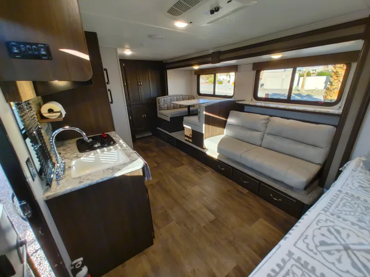 Inside this RV rental: a compact kitchen area with sink and stovetop, plus comfy dinette and sofa seating.. Keystone RV Springdale 2020