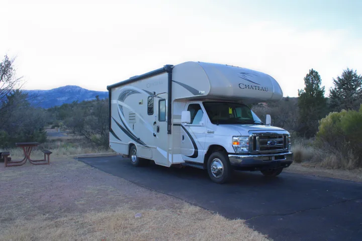 A white Chateau RV rental is parked on a paved spot at a scenic campsite with mountains in the distance and a picnic table nearby.. Other Other 2017