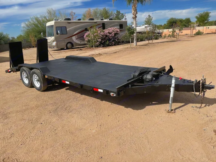 Heavy-duty car hauler trailer on a dirt lot, ideal for hauling. An RV rental motorhome is visible in the background.. Big Tex 20" Flatbed 2014