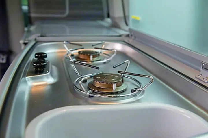 Compact RV rental kitchenette features a two-burner stove and sink, perfect for on-the-road cooking.. Volkswagen California Ocean 2024