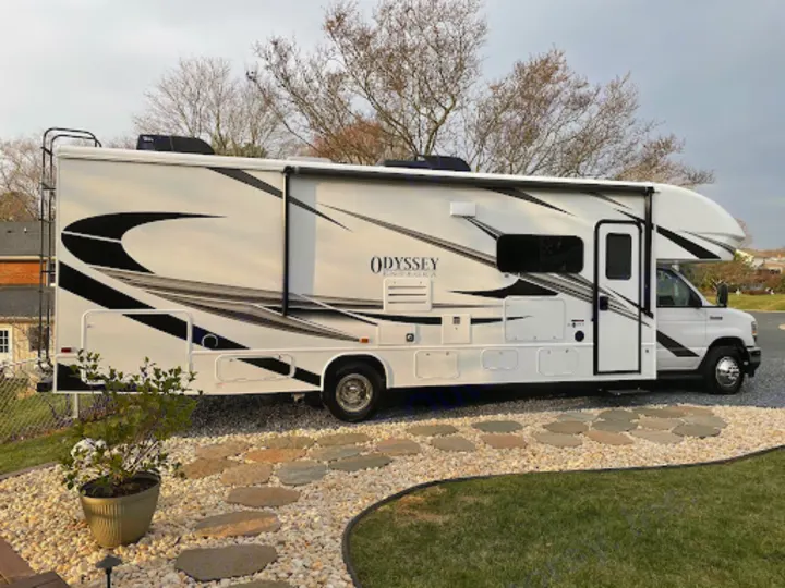 This bright white RV rental, an Odyssey Integra, is parked on a neat gravel path with stepping stones, ready for travel.. Entegra Coach Odyssey 2022