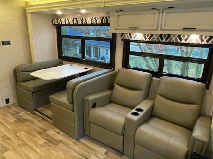 Comfortable RV rental interior with a U-shaped dinette, two recliners, and bright windows. Perfect for your next trip.. Entegra Coach Odyssey 2022