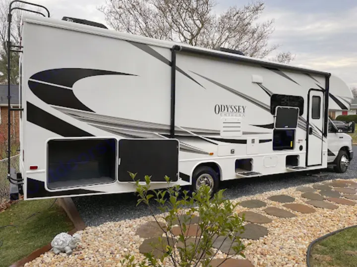 Spacious white Class C RV with storage bays open, parked on gravel. Perfect for your next rv rental adventure!. Entegra Coach Odyssey 2022