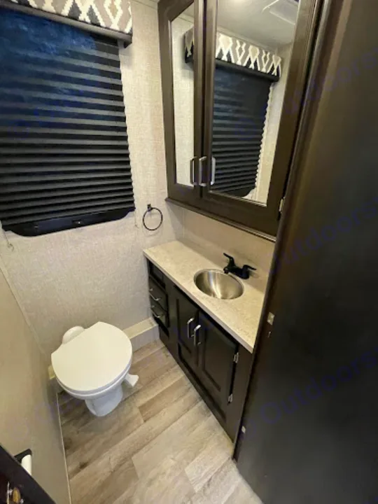 RV rental bathroom interior: toilet, sink, vanity, mirror, and window with blinds. A compact and functional space.. Entegra Coach Odyssey 2022