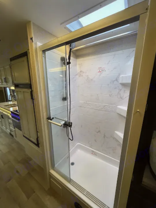 Inside a modern rv rental: a bright, glass-enclosed shower with a skylight, adjacent to a compact kitchen with light cabinets.. Entegra Coach Odyssey 2022