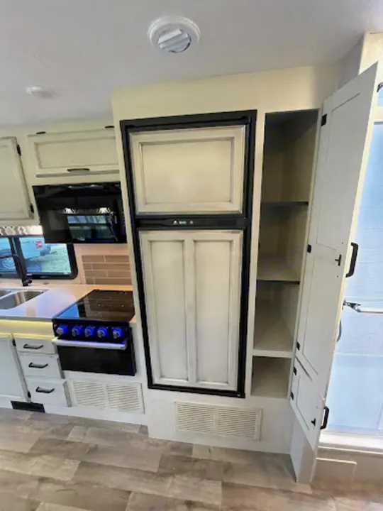 Modern RV rental kitchen with light cabinets, a large refrigerator, stove with blue lights, and pantry storage.. Entegra Coach Odyssey 2022