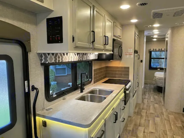 Step inside this bright RV rental, showcasing a fully equipped kitchen with a sink, stove, and microwave, leading to a cozy bedroom.. Entegra Coach Odyssey 2022
