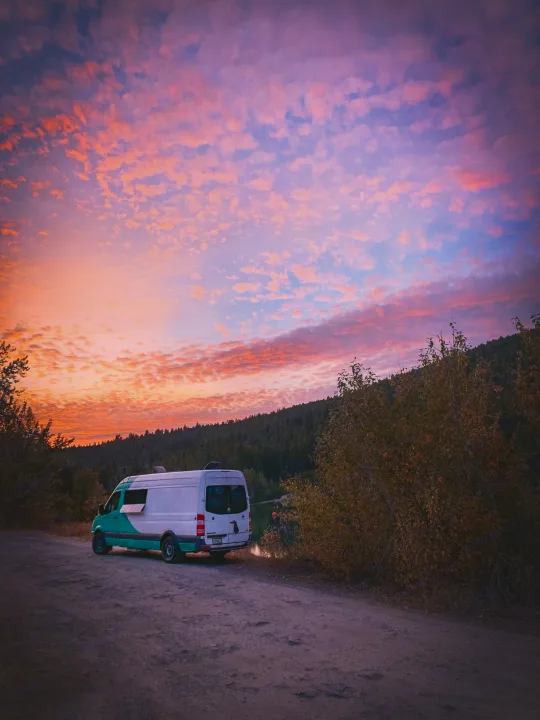 RV rental adventure: a teal and white camper van parked lakeside on a dirt road under a stunning pink and orange sunset.. Mercedes-Benz sprinter 2008
