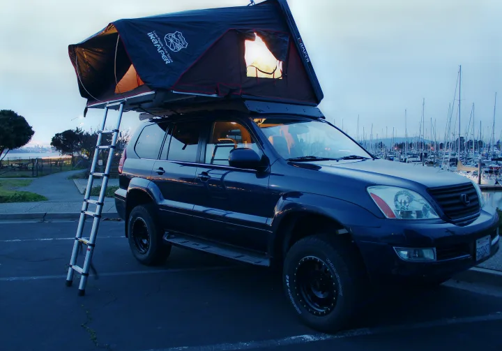 Dark SUV with illuminated iKamper roof-top tent and ladder, parked by a marina, similar to an RV rental setup.. Other Other 2004