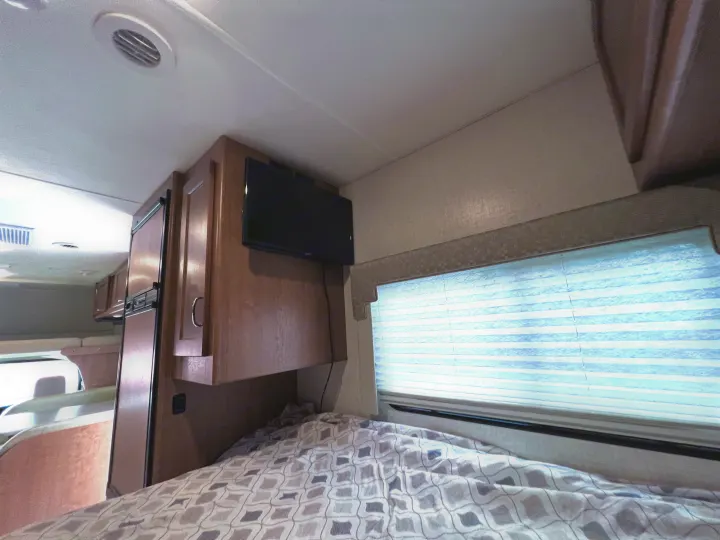 Cozy RV rental sleeping nook: A bed with patterned comforter, mounted TV, and window with blinds.. Winnebago Minnie Winnie 2020