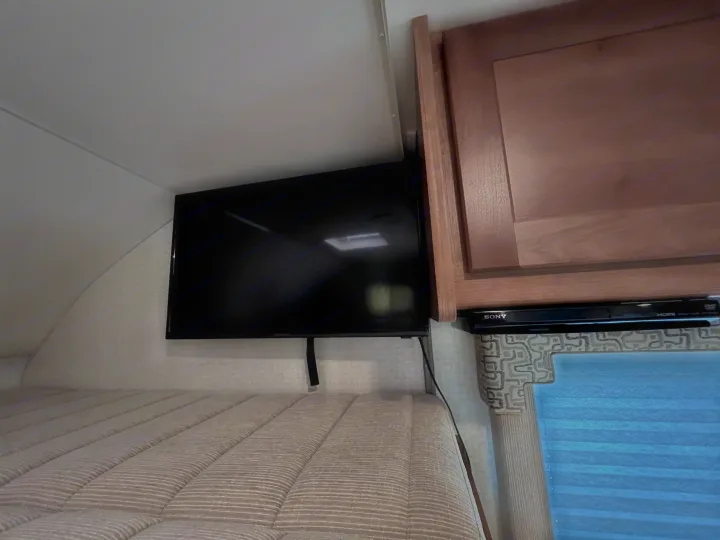 Enjoy an RV rental! This cozy sleeping area features a bed, wall-mounted TV, and DVD player for entertainment.. Winnebago Minnie Winnie 2020