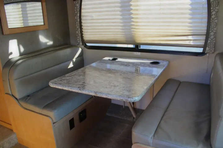 This RV rental interior showcases a cozy dinette area with cushioned benches, a table with cup holders, and a window with blinds.. Other Other 2017