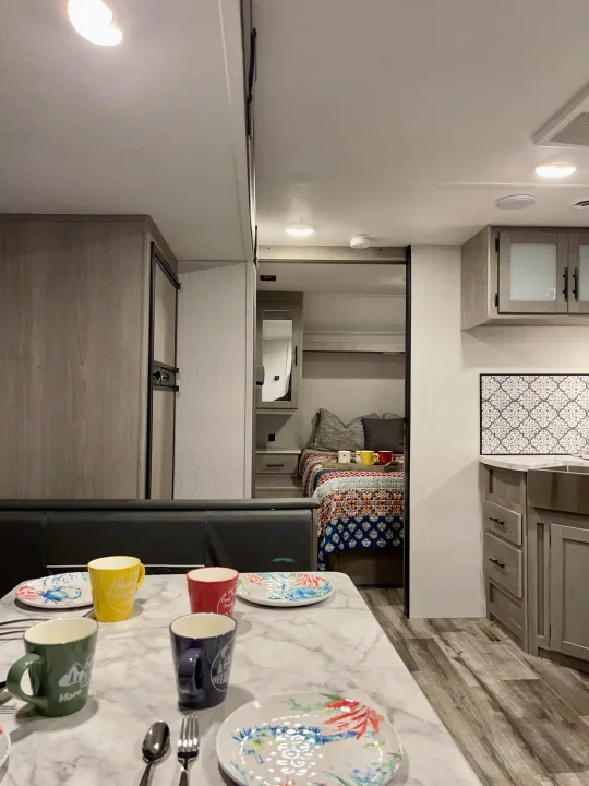 This modern rv rental features a cozy dining area with colorful mugs, a functional kitchen, and a comfortable bedroom.. Coleman Lantern 2022